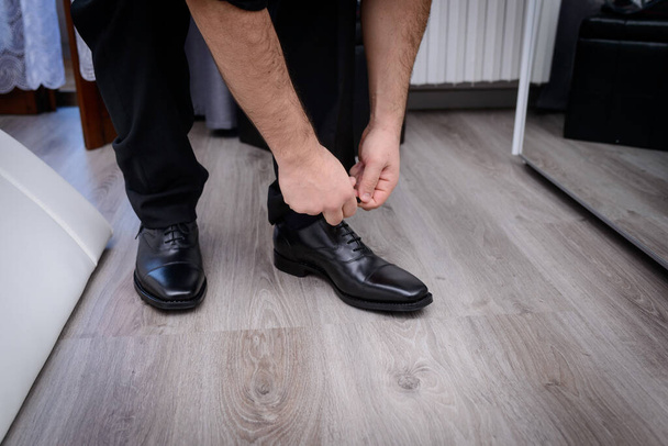 Cropped shot of a man in black tying his shoes in front of a mirror - Foto, Imagen