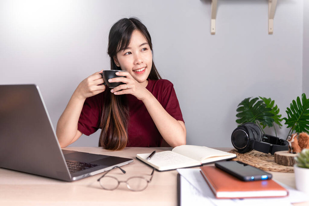 Mujer asiática pensativa es relajarse en el escritorio de trabajo de forma remota desde casa con el ordenador portátil para comunicarse en Internet con el cliente, E aprender a enseñar en el chat en línea, cuarentena concepto de Coronavirus
 - Foto, imagen