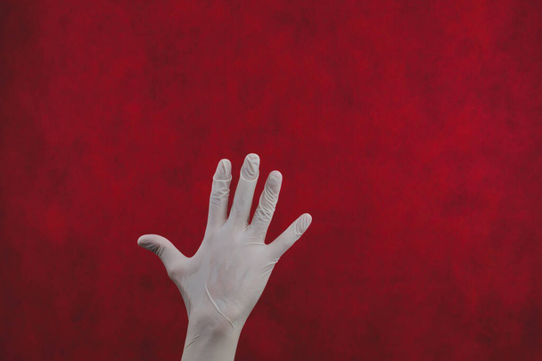 Hand in protective glove on a red background. gesturing hand in white medical glove - Φωτογραφία, εικόνα
