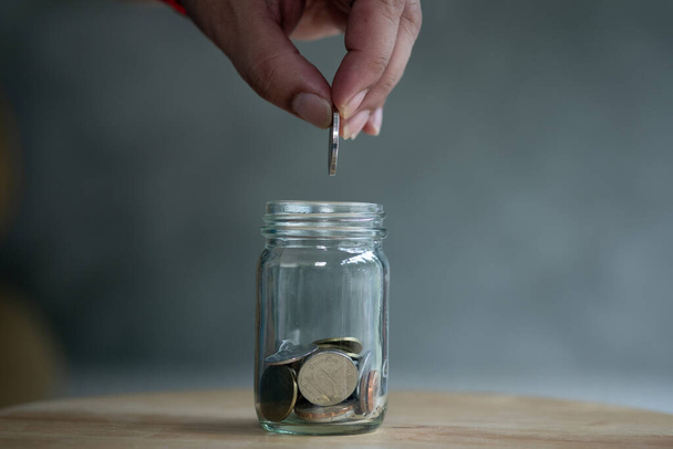 Man hand put Thai coin in to jar glass. Saving money concept. - Foto, afbeelding