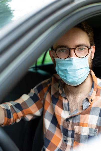 Male driver with protective gloves and a face mask, sitting in a car. Everyday prevention against infections and viruses.  - Foto, imagen