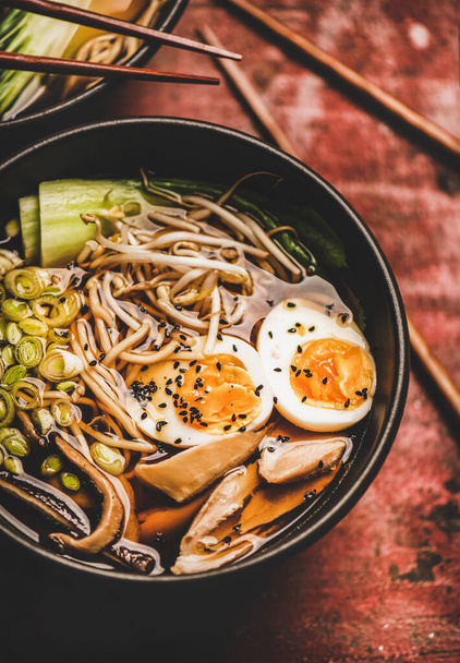 Traditional japanese Ramen soup with chicken meat and shiitake mushrooms in black bowls and bamboo chopsticks over dark red wooden table background, top view. Japanese cuisine concept - Foto, Imagem
