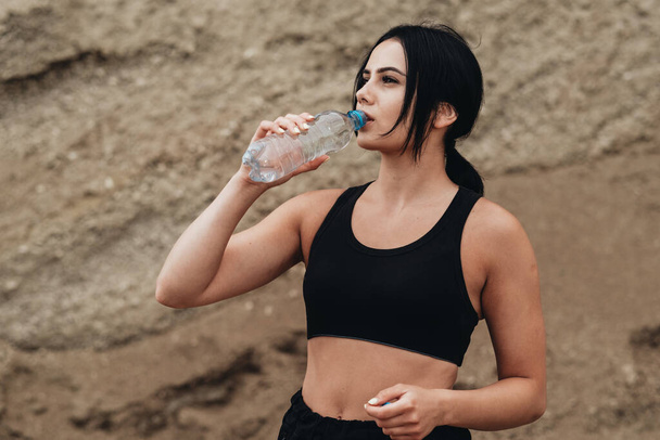 Молодая спортсменка в черном спортивном костюме пьет воду здоровый образ жизни и на открытом воздухе концепция тренировки
 - Фото, изображение