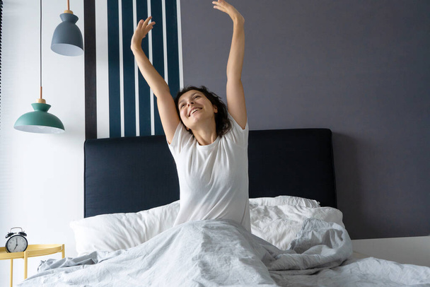 Beautiful girl wakes up in a good mood in a stylish apartment. Stretches with a smile starting the day. - Photo, image
