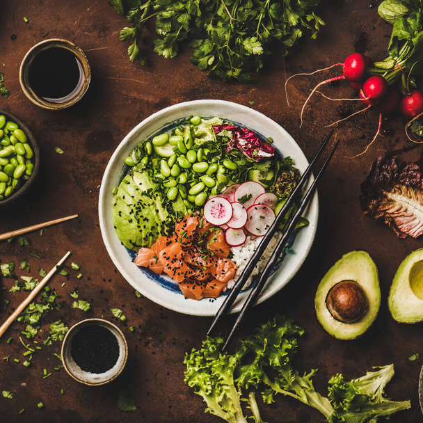 Healthy lunch, dinner. Flat-lay of salmon poke bowl or sushi bowl with vegetables, greens, sushi rice, soy sauce over rusty table background, top view, square crop. Traditional Hawaiian cuisine - Foto, Bild