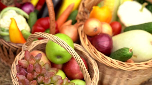 Summer fruits and vegetables in baskets. Abstract blurred image with apples, grapes, cauliflower, carrots, eggplant, peppers, onions, cucumbers, corn and zucchini in wicker baskets. Close-up shot - 写真・画像