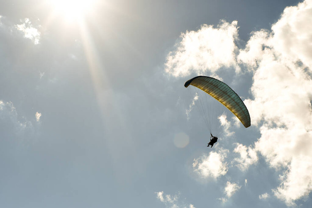 silhouette of a girl flying in a paragliding with a blue sky with clouds in the background on a sunny day - Photo, Image