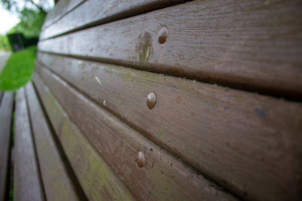 Zblízka stará dřevěná hnědá lavička. V pozadí rozmazaný zelený park. Koncept. - Fotografie, Obrázek