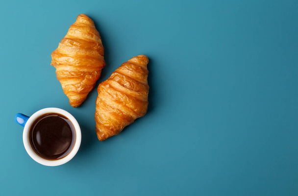 Horizontal copy space with two croissants and cup of fresh fragrant coffee at blue background. Concept of modern minimal breakfast food. Top view, flat lay - Photo, Image