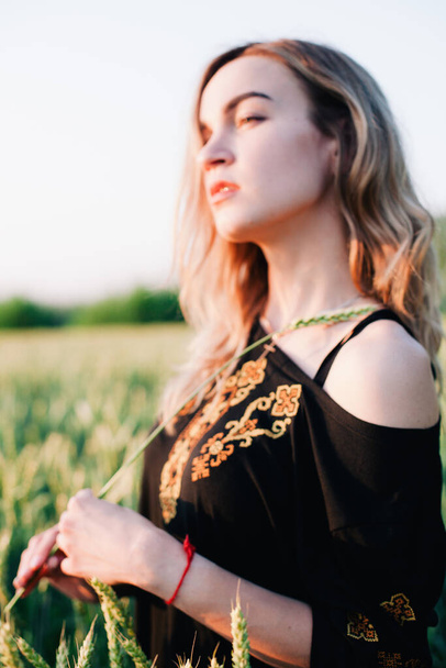 Young, slender girl embroidered dress in a large wheat field at sunset - Foto, Bild