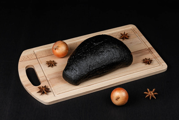 tuoretta mustaa ruisleipää leikkuulaudalla mausteita sirotellaan musta puinen pöytä - Valokuva, kuva