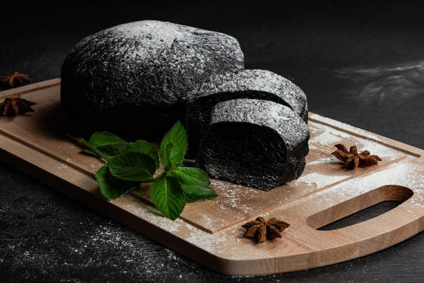 tuoretta mustaa ruisleipää leikkuulaudalla mausteita sirotellaan jauhoja musta puinen pöytä - Valokuva, kuva