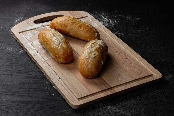 fresh white bread on a cutting board with  with flour on a black wooden table - Photo, Image