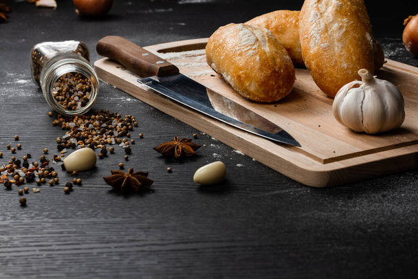 čerstvý bílý chléb na řezací desce s koření posypané moukou na černém dřevěném stole - Fotografie, Obrázek