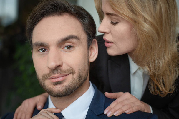 Woman stroking male shoulders. Passionate couple of two Caucasian business people. Close up portrait. Selective focus on male face. Flirt or love affair at job - Zdjęcie, obraz