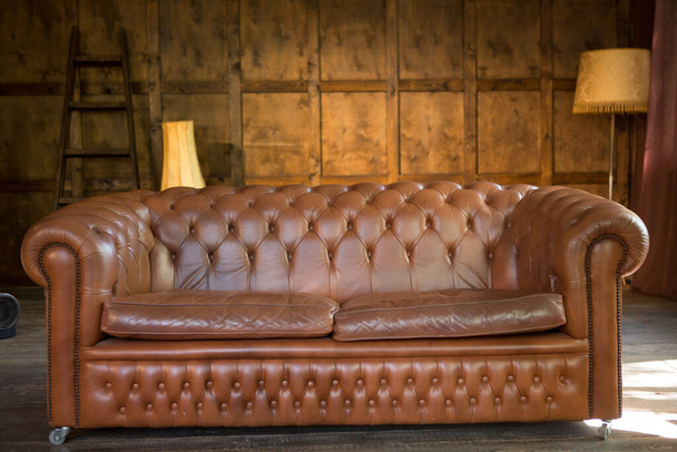 Solides Ledersofa in einem Holzinterieur. Braune Couch im Wohn- oder Büroloft-Stil - Foto, Bild