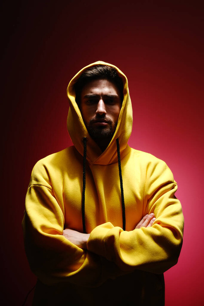A young man of 25-30 years old in a yellow sweatshirt is standing against a red wall.  - Photo, Image