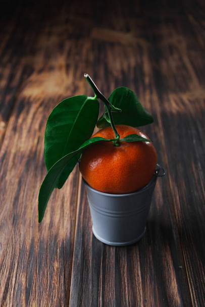 Fresh tangerines with leaves in a bucket on a wooden old background - Photo, Image