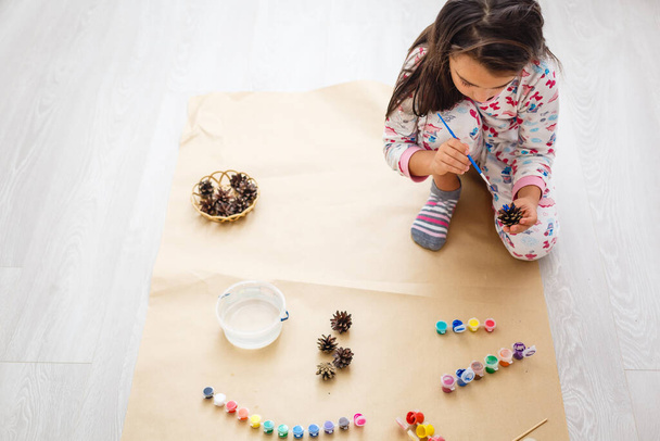 Симпатична маленька дівчинка, що розмальовує натуральну конусну ялину, щоб створити квітку, набір пензлів, фарб, природних осінніх матеріалів, створити весело і легко з дітьми, для дитячого садка
 - Фото, зображення