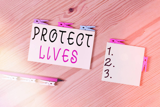 Szóírás szöveg Protect Lives. Üzleti koncepció, hogy fedezze vagy védje a kitettség sérülés vagy megsemmisülés Színes ruhacsap papírok üres emlékeztető fa padló háttér iroda. - Fotó, kép