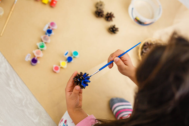 栗や松ぼっくりやアコーンから秋の装飾を作る小さな子供は - 写真・画像