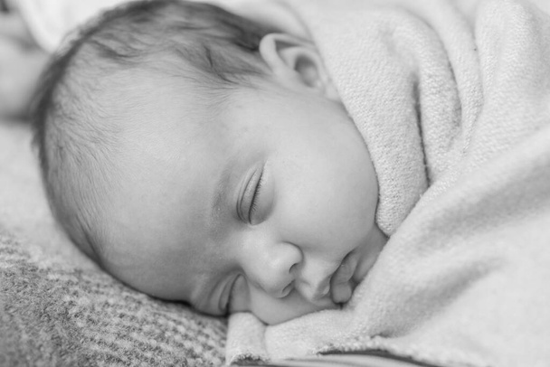 infancy, childhood, development, medicine and health concept - close-up smiling face of newborn sleeping baby girl lying on stomach covered wrapped in warm soft blanket. Black and white Copy space - Zdjęcie, obraz
