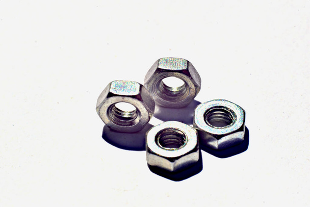 On a white table are four nuts for bolts. High quality photo - Photo, Image