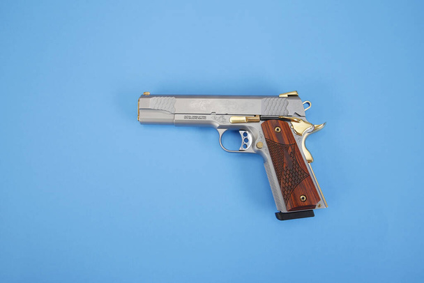 pistol or gun inlaid with wood and gold isolated on a blue background. weapon concept. protection and violence. - Photo, Image