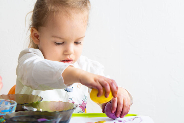 Hyvää pääsiäistä. Pikkutyttö maalasi munia. Lapsi valmistautuu pääsiäiseen. Maalattu käsi. Sormimaalaus. Taiteen ja käsityön käsite. Perinteinen kevätloma ruoka - Valokuva, kuva