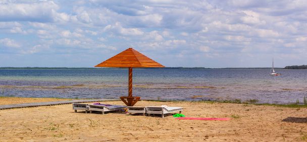 Tahta şemsiye ve güneşlik ya da göl kenarındaki boş sahildeki plaj şezlongu. - Fotoğraf, Görsel
