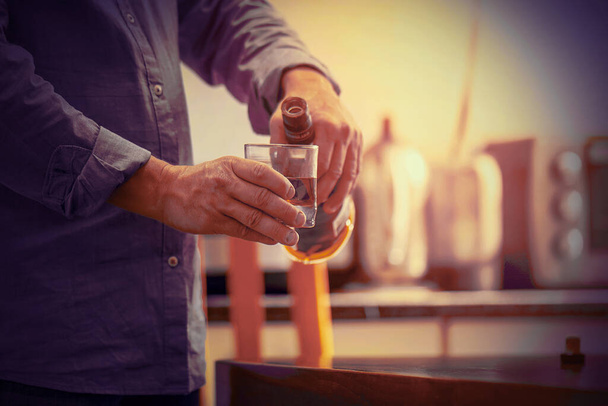 Mains d'homme caucasien âgé avec bouteille de whisky sur la cuisine. Le concept d'ivresse et d'alcoolisme. Père alcoolique. Tonique - Photo, image