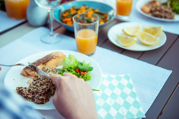 Close up photo of hands young man eating fresh salad, quinoa and fish with family on terrace at home - Valokuva, kuva