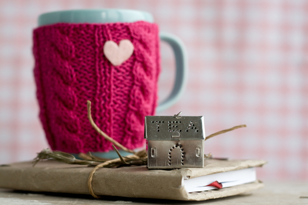 Xícara azul em um suéter rosa em pé em um caderno velho
 - Foto, Imagem