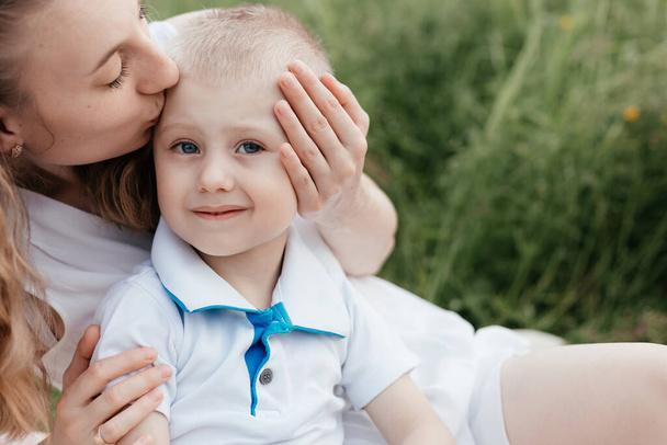 Mother kissing her little son with blue eyes at the background of the field. Mother and son. Happy family - Photo, Image