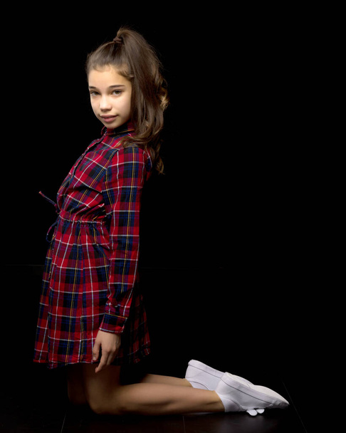 A little girl is kneeling on a black background in the studio. - Zdjęcie, obraz
