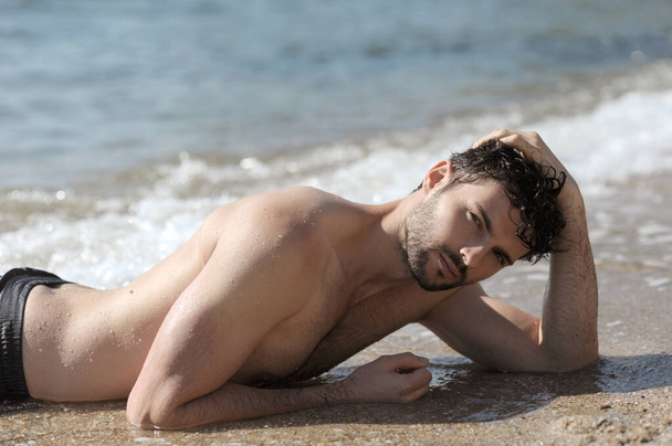 Young stylish man outdoor topless laying portrait near the sea - Photo, Image