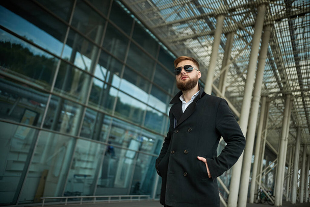 Success. Stylish young bearded man in coat, sunglasses businessman standing - Foto, Bild
