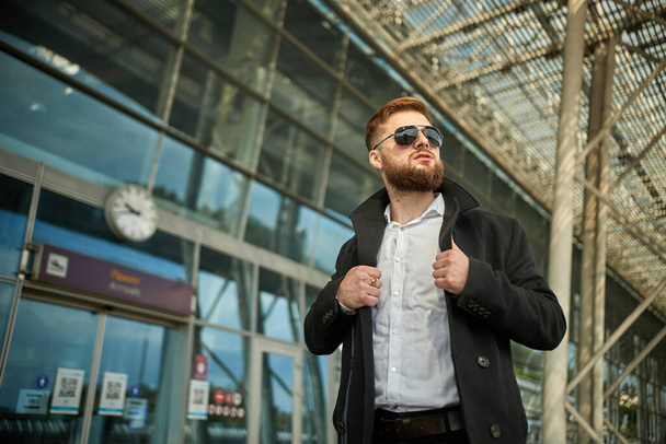 Red-head guy in sunglasses adjusting collar with both hands, man looking away - Photo, Image