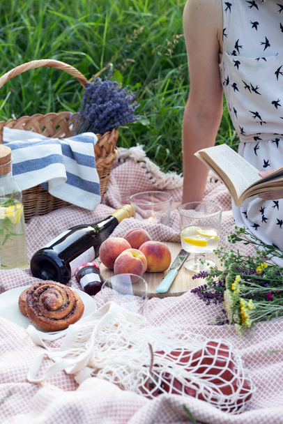 Summer - lemonade with lemon and mint with wine, peaches, cinnamon rolls, candles and a bouquet and a baske - Foto, afbeelding
