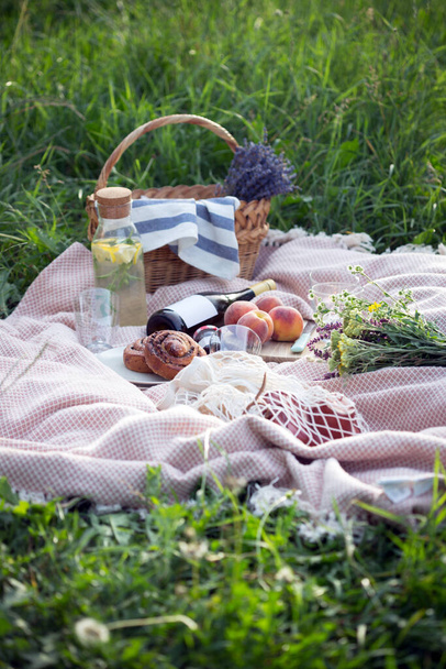 Summer - lemonade with lemon and mint with wine, peaches, cinnamon rolls, candles and a bouquet and a baske - Фото, изображение