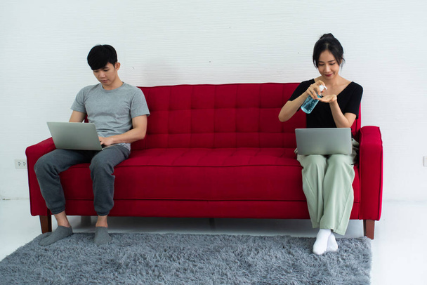 Happy Asian couple cleaning hands with sanitizer alcohol gel while sitting working together on sofa at home. - Fotoğraf, Görsel