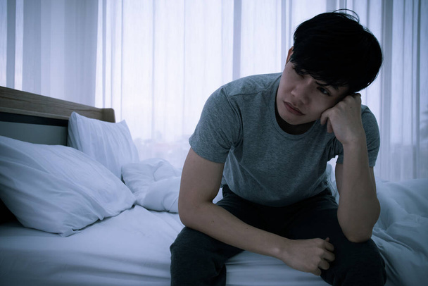 Stressed Asian young man sitting alone on bed. Bad relationship or bankrupt problem and sickness concept. - Foto, Imagem