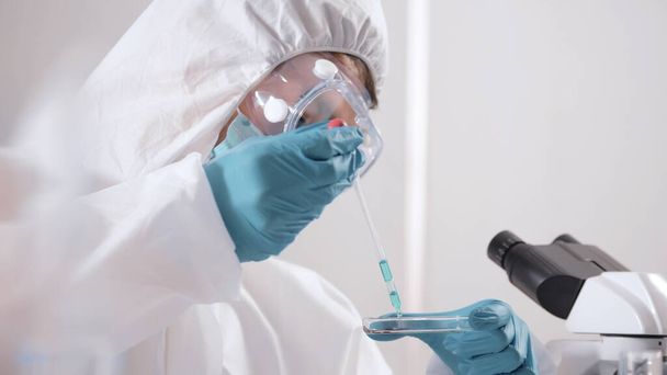 A PPE lakosztályban dolgozó tudós egy folyadékot vizsgál egy kémcsőben a laboratóriumban.. - Fotó, kép