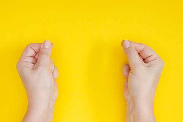 Hands with clenched fingers in a pinch on a yellow background - 写真・画像