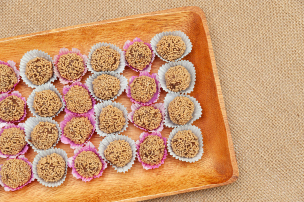 Traditional Brazilian homemade candy called "Brigadeiro de Amendoim" in Brazilian Portuguese. Made with crushed peanuts, margarine and condensed milk. Top view. Copy space. Jute fabric background. - Photo, Image