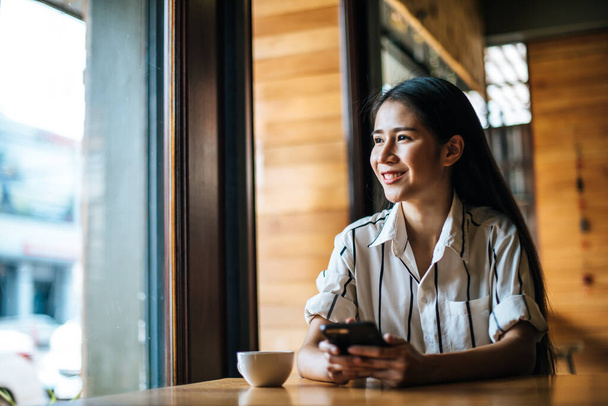 Egy nő ül és játssza az okos telefonját a kávézóban. - Fotó, kép