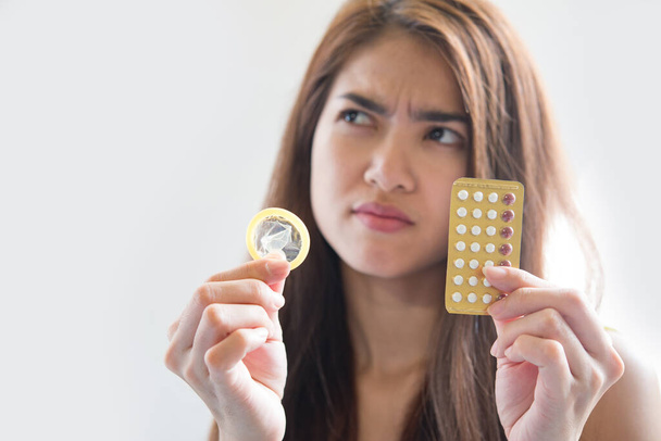 Mujer joven sosteniendo condón y píldoras anticonceptivas previenen el embarazo
 - Foto, imagen