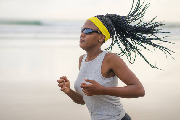 determined African American woman running on the beach - young attractive and athletic black girl training outdoors doing jogging workout at the sea in fitness and healthy lifestyle concept - Fotografie, Obrázek