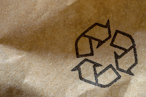 újrahasznosítási szimbólum barna újrahasznosított papírra nyomtatva, kép másolási hellyel, sekély mélységélesség - Fotó, kép