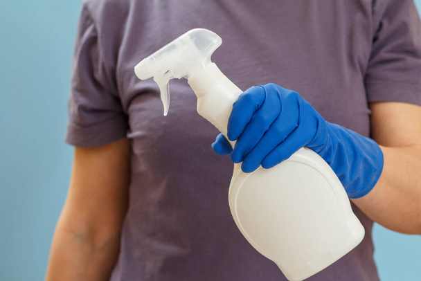 Vrouw in een t-shirt met een plastic fles wasvloeistof op de blauwe achtergrond. Was- en reinigingsconcept. - Foto, afbeelding